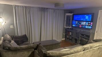 Een woonkamer met een grijze zithoek, een flatscreen televisie en een boekenkast.