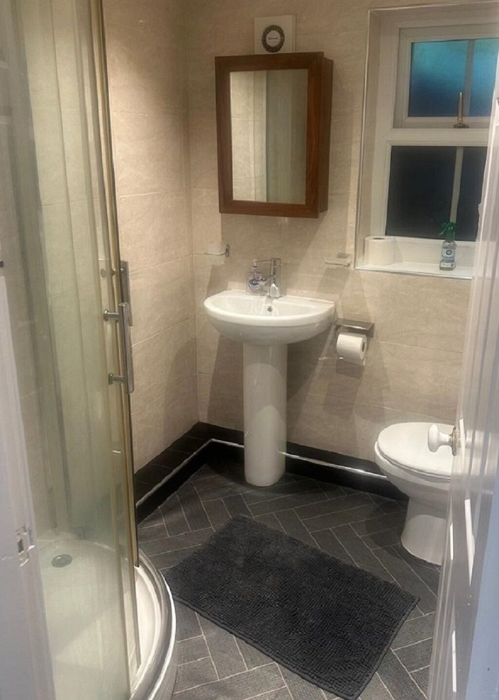 Et badeværelse med brusekabine i glas, et konsolbord med vask og et toilet.