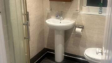 Et badeværelse med brusekabine i glas, et konsolbord med vask og et toilet.
