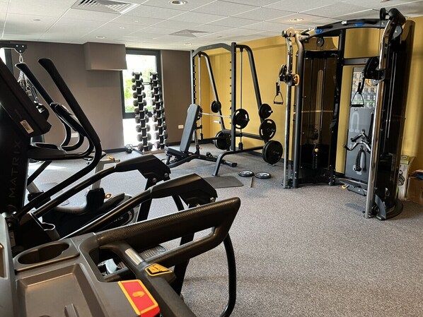 Une salle de sport équipée de tapis de course, d’appareils de musculation et de poids libres.