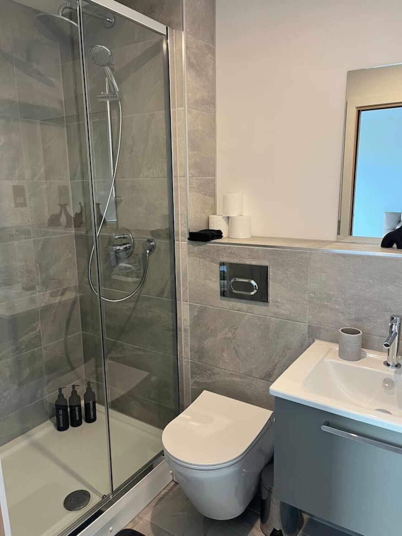 A modern bathroom with a glass-enclosed shower, a toilet, and a sink with a mirror above.