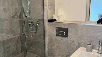 A modern bathroom with a glass-enclosed shower, a toilet, and a sink with a mirror above.