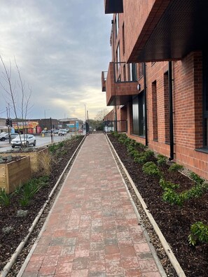 Un bâtiment en briques avec un trottoir dallé menant à un espace de stationnement.