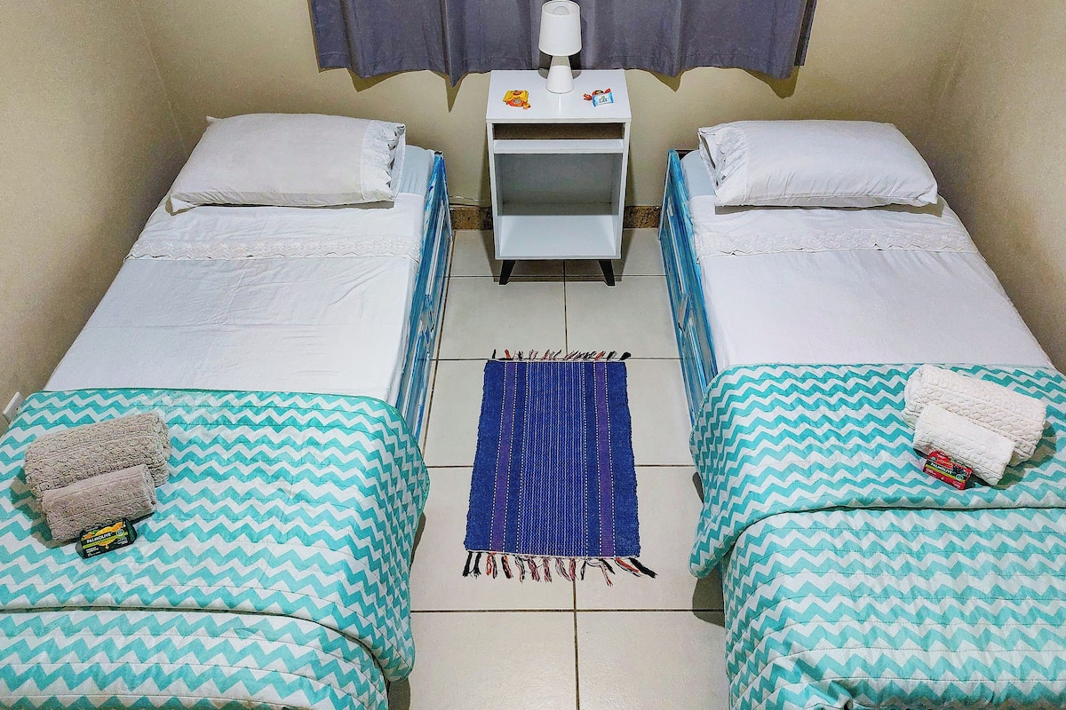 A small, clean room with two single beds, a nightstand with a lamp, and a blue rug.