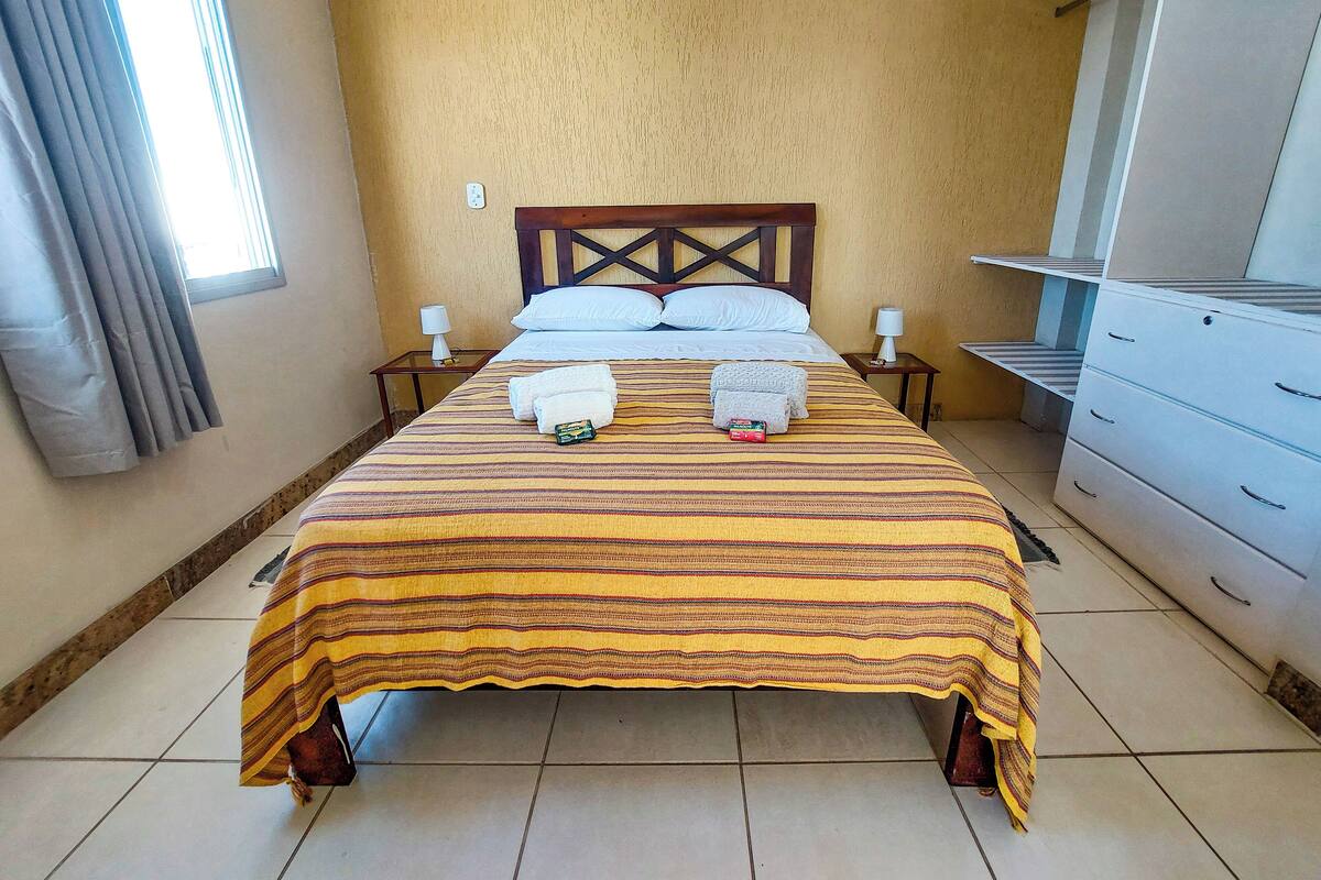 A hotel room with a bed, two bedside tables, a wardrobe, and a window with curtains.
