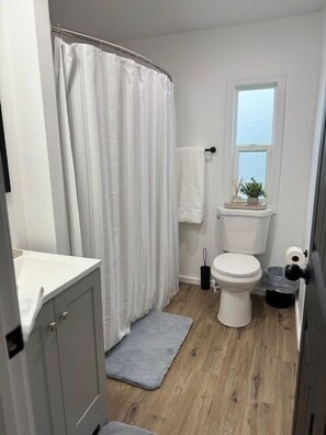 Un baño con cortina de ducha, inodoro, lavamanos y una ventana pequeña.