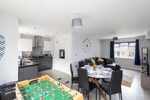Una cocina moderna con mesa de futbolín, comedor con mesa para cuatro y sala de estar con sofá y reloj en la pared.