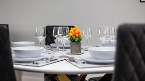 Une table à manger dressée avec de l’assiette blanche, des verres transparents et une petite plante en pot.