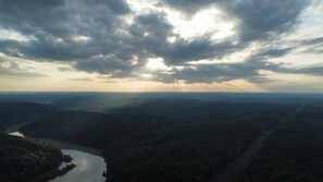 A panoramic view of a mountainous landscape with a river, dense forest, and a cloudy sky.