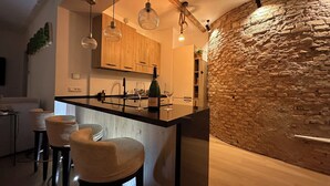 A modern kitchen with a central island, bar stools, hanging pendant lights, and a stone accent wall. - House in the shadow of the Colosseum (Roma)