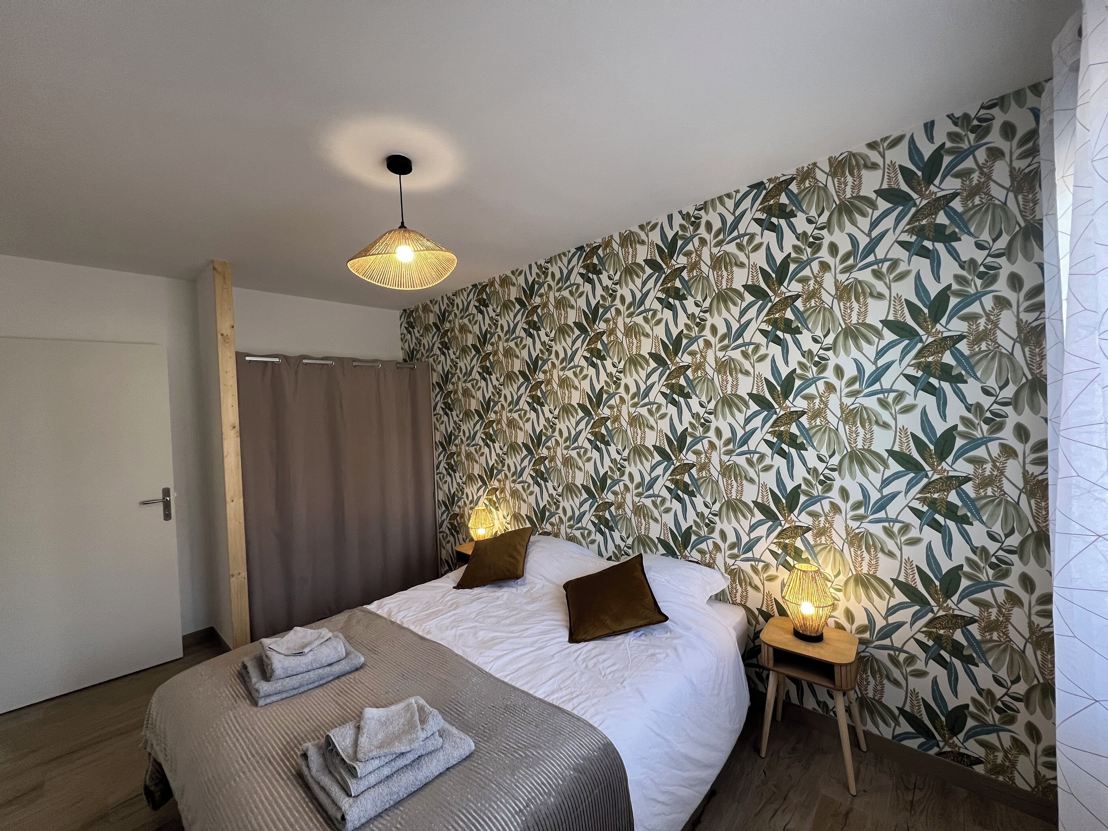 A bedroom with a bed, two bedside lamps, a wooden nightstand, and a curtain.