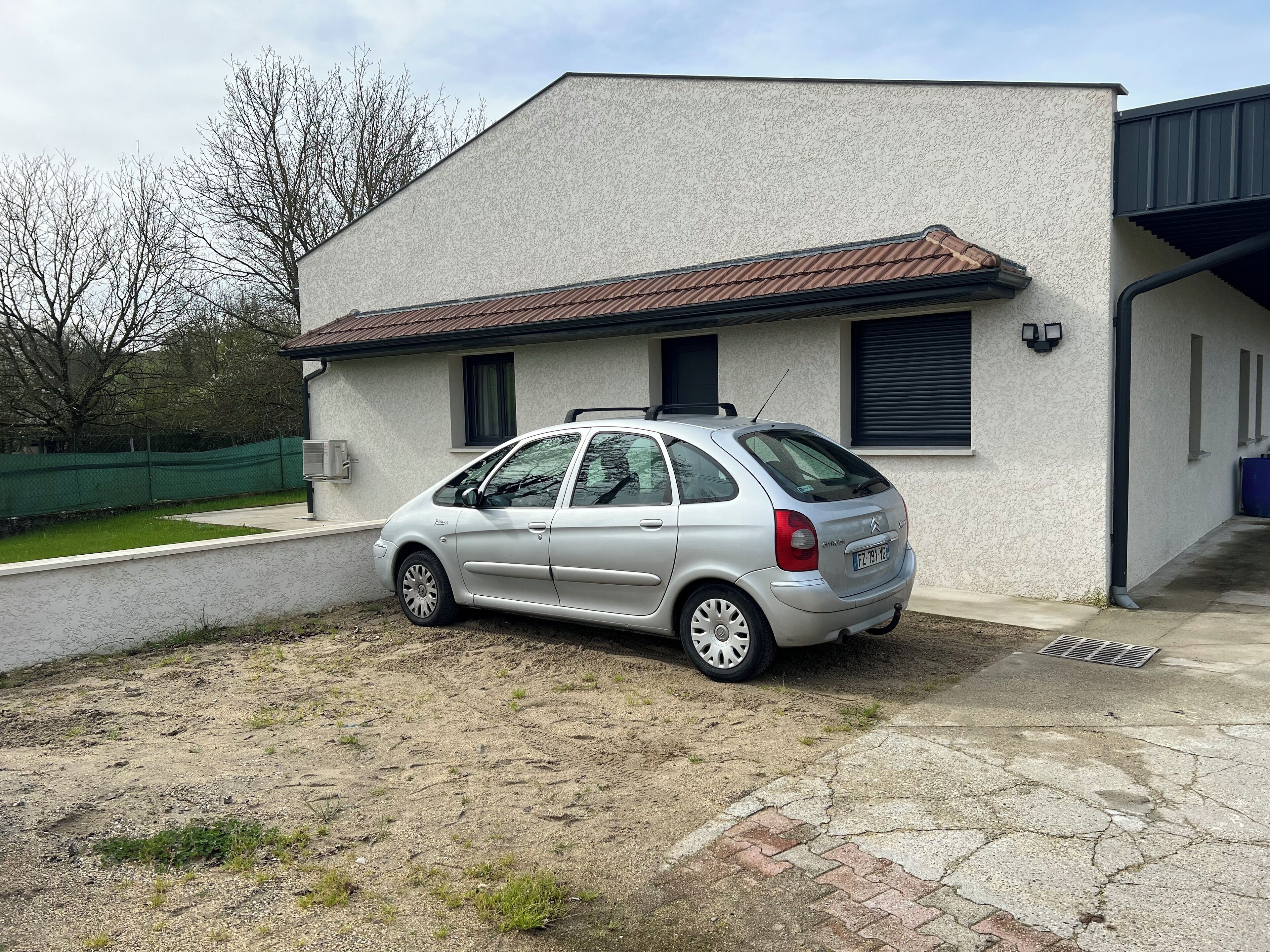 Ein silbernes Auto vor einem weißen Gebäude mit einem braunen Dach.