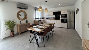 A modern kitchen with a dining area, featuring a wooden table, chairs, and pendant lights. - le Cocon Vézerontin (Vézeronce-Curtin)