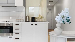 A modern kitchen with white cabinetry, a built-in oven, a coffee maker, and a vase with white flowers. - 1BR Apartment on North Terrace (Adelaide)