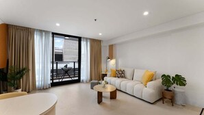 A modern living room with a sofa, coffee table, and a dining table. - 1BR Apartment on North Terrace (Adelaide)