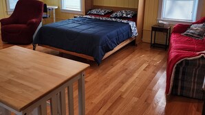 Ein Zimmer mit einem Bett, einem roten Sessel, einem kleinen Tisch und einer hölzernen Bank.