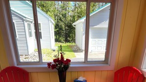 Ein Zimmer mit zwei roten Stühlen, einem kleinen Tisch mit Blumenvase und einem Fenster mit Blick auf eine Wohngegend.
