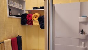 Ein Badezimmer mit Toilette, Dusche und einem Ablagebereich mit Handtüchern und Pflegeprodukten.
