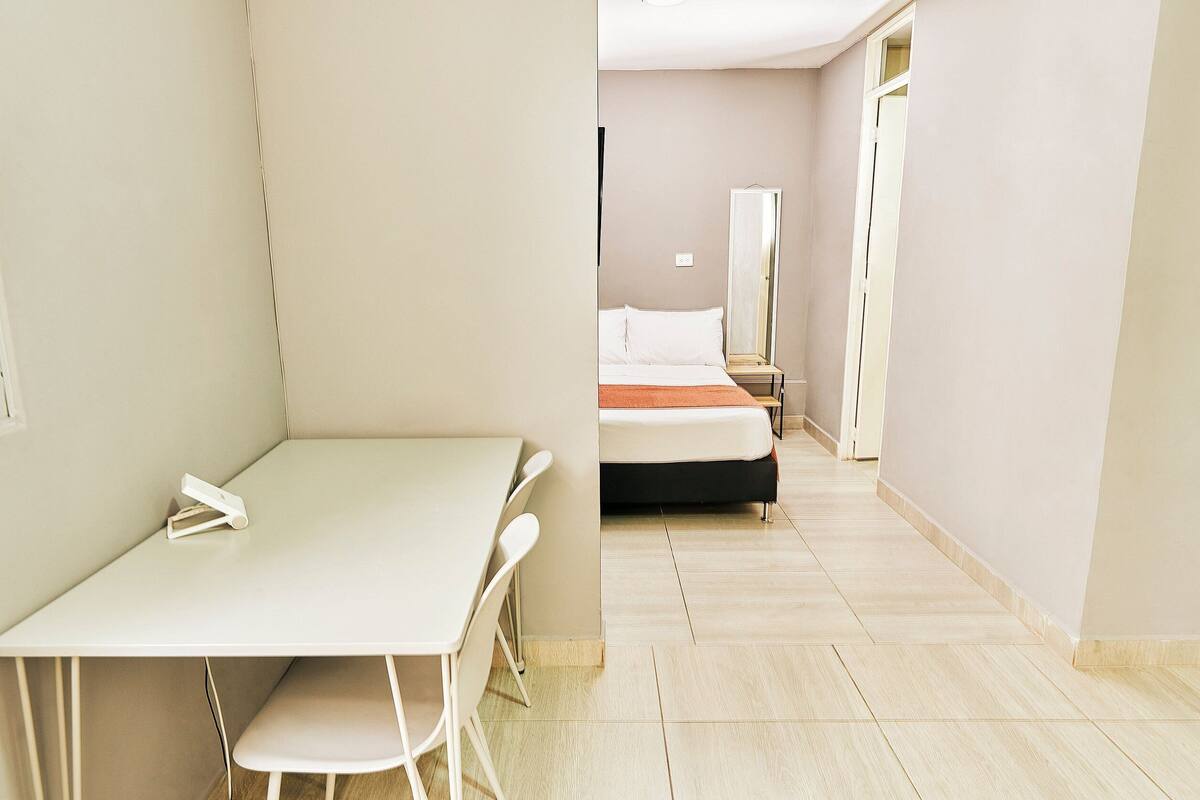 Ein kleiner, gut beleuchteter Raum mit einem Bett, einem Nachttisch und einem Sessel.