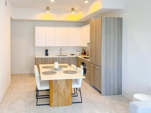 A modern kitchen with white cabinets, a wooden dining table, and a built-in oven.