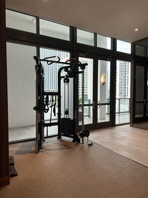 A gym with exercise equipment, large windows, and a view of tall buildings.