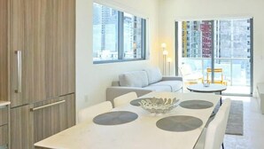 A modern kitchen with a dining table, white chairs, and a view of the city through large windows. - Sleek Urban Living Stylish 1BR in Brickell (Miami)