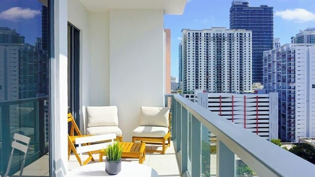 A balcony with a white table and chairs, a potted plant, and a cityscape view. - Sleek Urban Living Stylish 1BR in Brickell (Miami)