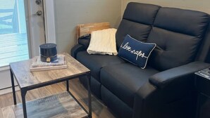 A modern living room with a black leather sofa, a small wooden coffee table, and a wall-mounted air conditioner. - Riverfront Tiny Home - Amazing Views (Strawberry Plains)