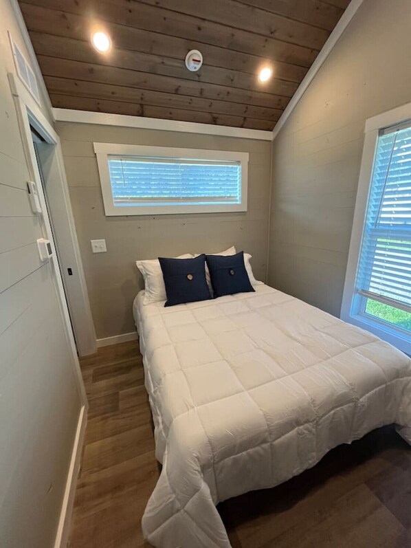 A bedroom with a bed, a window with blinds, a ceiling light, and a thermostat.