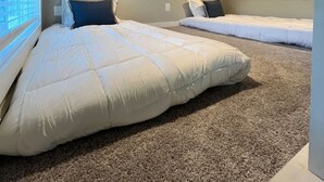 A bedroom with a sloped ceiling, two beds, a window, and a carpeted floor. - Riverfront Tiny Home - Amazing Views (Strawberry Plains)