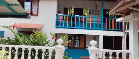 A two-story building with a balcony, potted plants, and a tiled entrance.