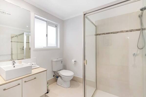 A modern bathroom with a glass-enclosed shower, a white sink, and a toilet. - Ocean55 Mooloolaba Holiday Home (Mooloolaba)