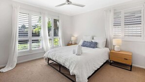 A bedroom with a bed, nightstands, a ceiling fan, and windows with blinds. - Ocean55 Mooloolaba Holiday Home (Mooloolaba)