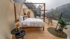 A tented bedroom with a bed, a small table, and a chair. - Kafen Hotel  (Juayua)