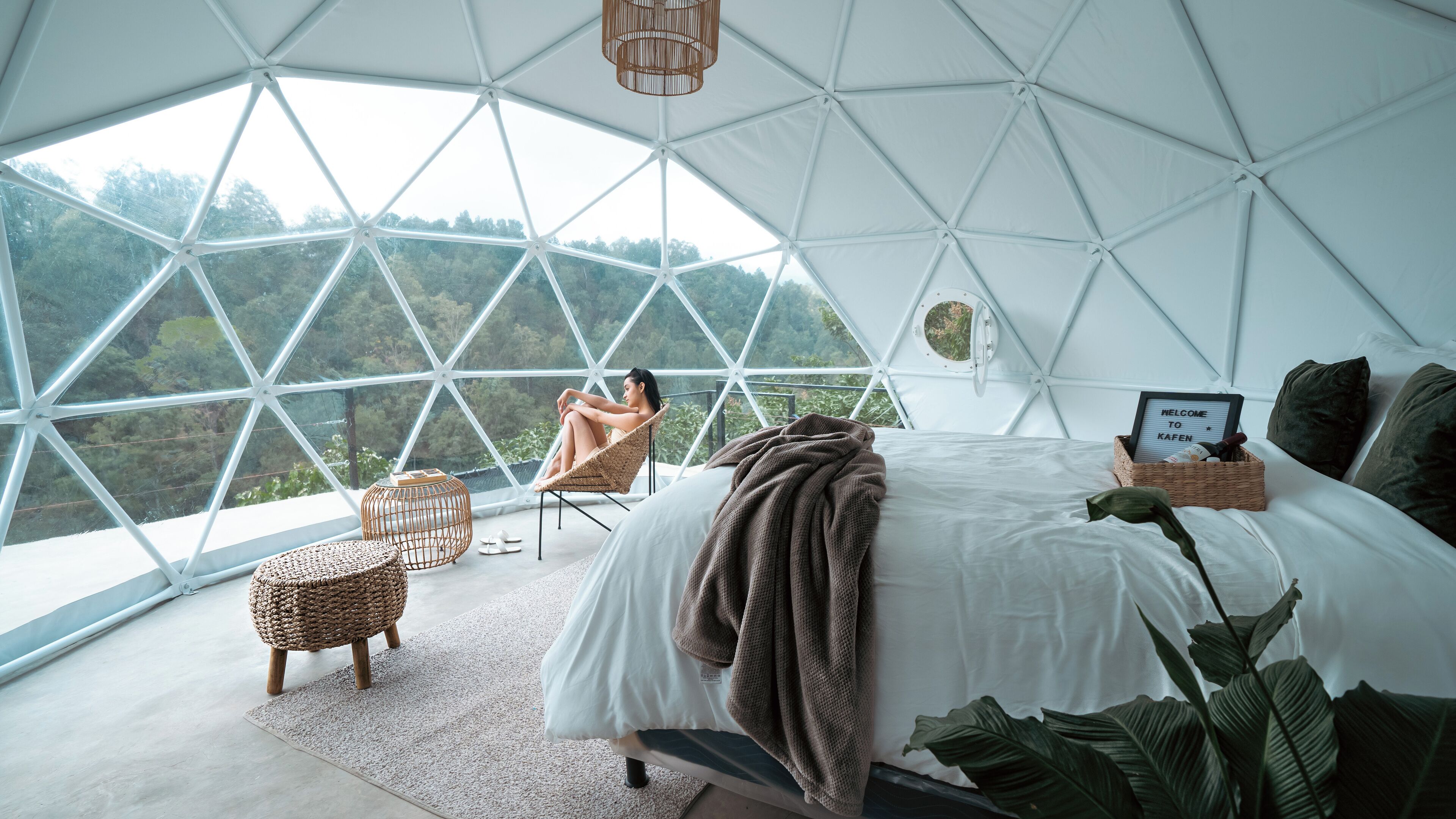 Een ruime, moderne slaapkamer met een groot bed, een comfortabele fauteuil en uitzicht op het bos door een koepelvormig dak.
