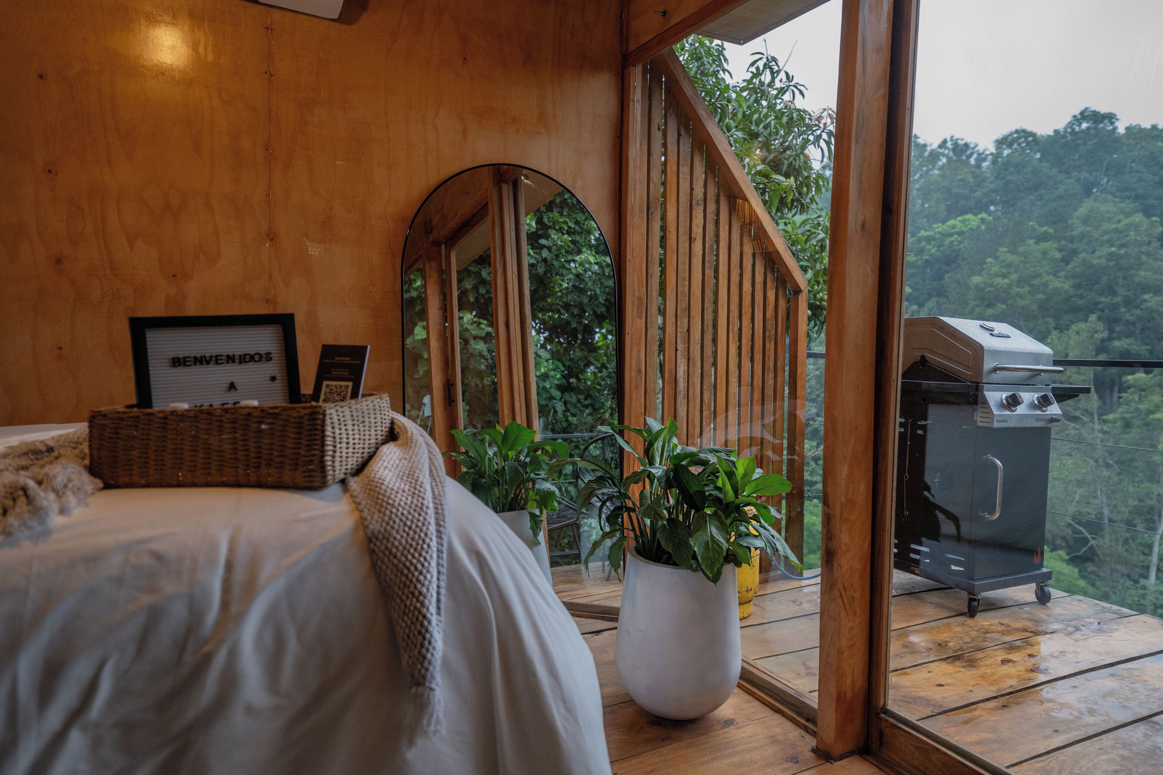 Quarto de cabana de madeira com cama, placa de boas-vindas, cesta de vime, planta em vaso e churrasqueira.