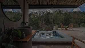 A spa area with a hot tub, wooden chairs, and a view of a forest. - Kafen Hotel  (Juayua)