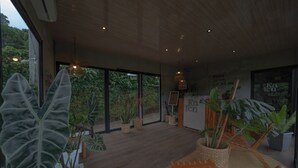 A modern interior with large windows, indoor plants, and a seating area. - Kafen Hotel  (Juayua)