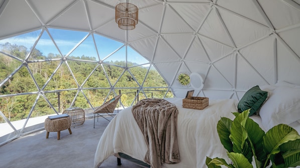 Una habitación tipo cúpula geométrica con cama, muebles de mimbre y vistas a un bosque.