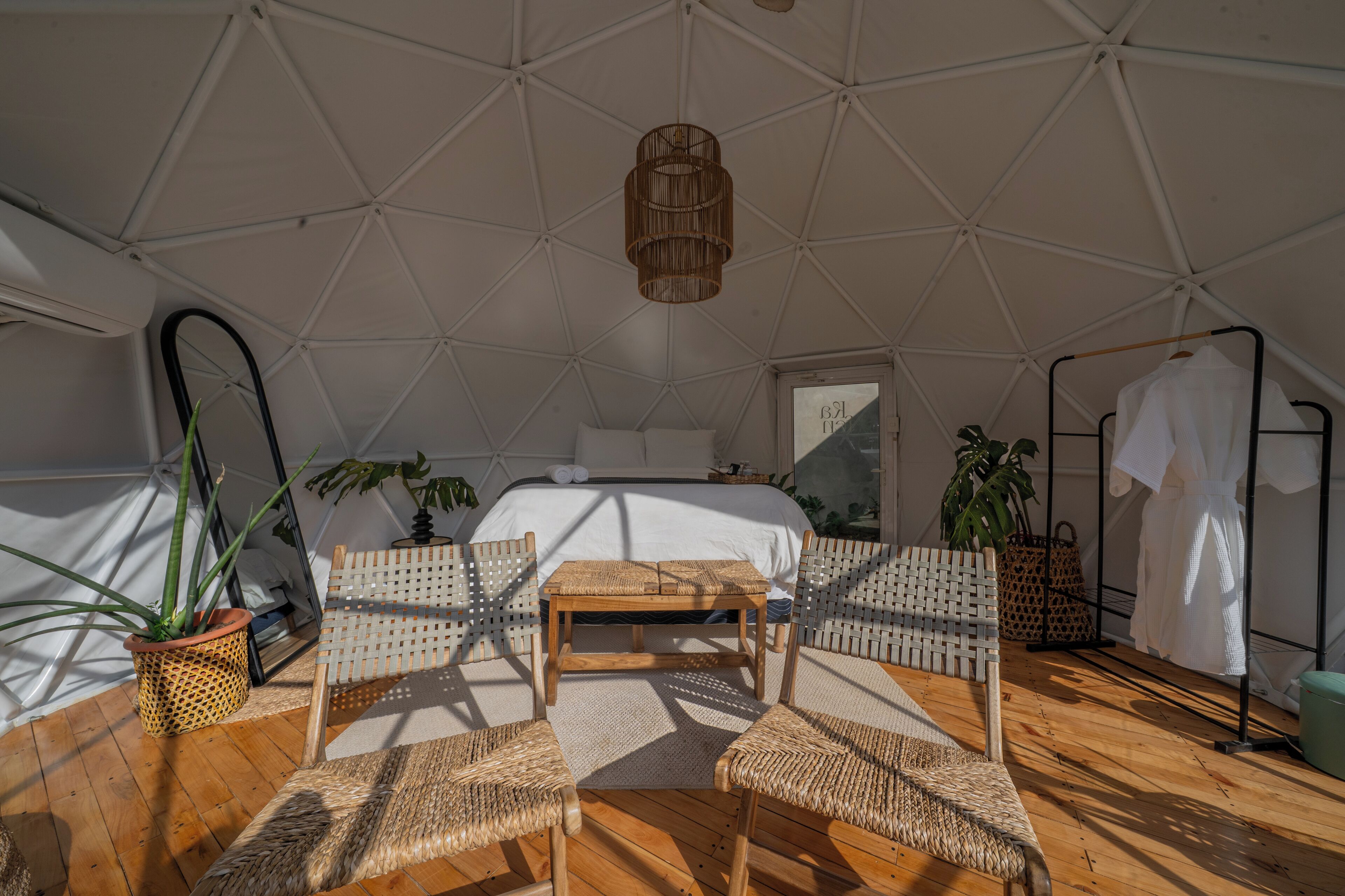 Una habitación tipo tienda de campaña con cama, muebles de mimbre y plantas en macetas.