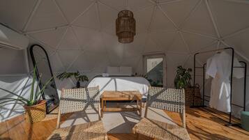 Una habitación tipo tienda de campaña con cama, muebles de mimbre y plantas en macetas.