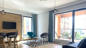 A modern living room with a sofa, two chairs, a TV, and a large window with curtains. - Modern Old Town 3 by Grand Apartments (Gdansk)