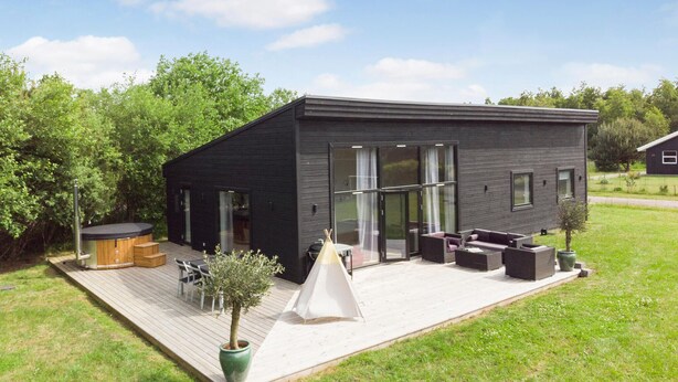 Ein modernes, schwarzes Haus mit einer Terrasse, Sitzgelegenheiten im Freien und einem Whirlpool.