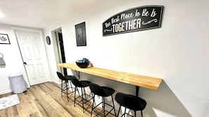 Una cocina con mostrador de madera, taburetes negros y un cartel en la pared.