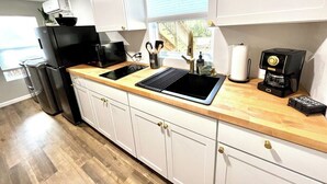Una cocina moderna con armarios blancos, encimera negra, un lavamanos, cafetera y una ventana con persianas.