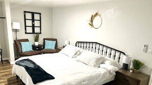Un dormitorio ordenado con una cama grande, mesitas de noche, una silla y un adorno en la pared.