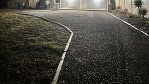 Una casa con entrada de grava, rodeada de árboles y una cerca.