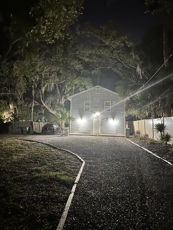 A house with a gravel driveway, surrounded by trees and a fence. - Renovated 2BR w/ Fire Pit, King Bed & Laundry · 8 Min to Speedway & Beach (Daytona Beach)