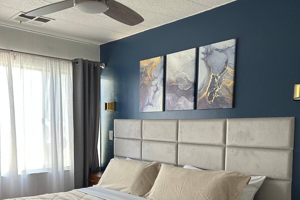 Una camera da letto con un letto, una ventola a soffitto, un comodino e opere d'arte alle pareti.