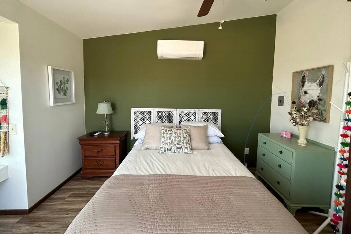 Una camera da letto con un letto, una ventola a soffitto, un comodino, una cassettiera e un condizionatore d'aria fissato al muro.